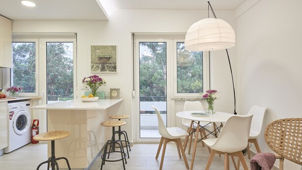 A modern kitchen with a dining area, large windows, and a hanging light fixture. - Light Apartment W/ Balcony Apartment by TimeCooler (Lisbon)