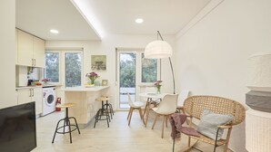 A modern kitchen with a washing machine, a dining area with a table and chairs, and a TV on a stand. - Light Apartment W/ Balcony Apartment by TimeCooler (Lisbon)
