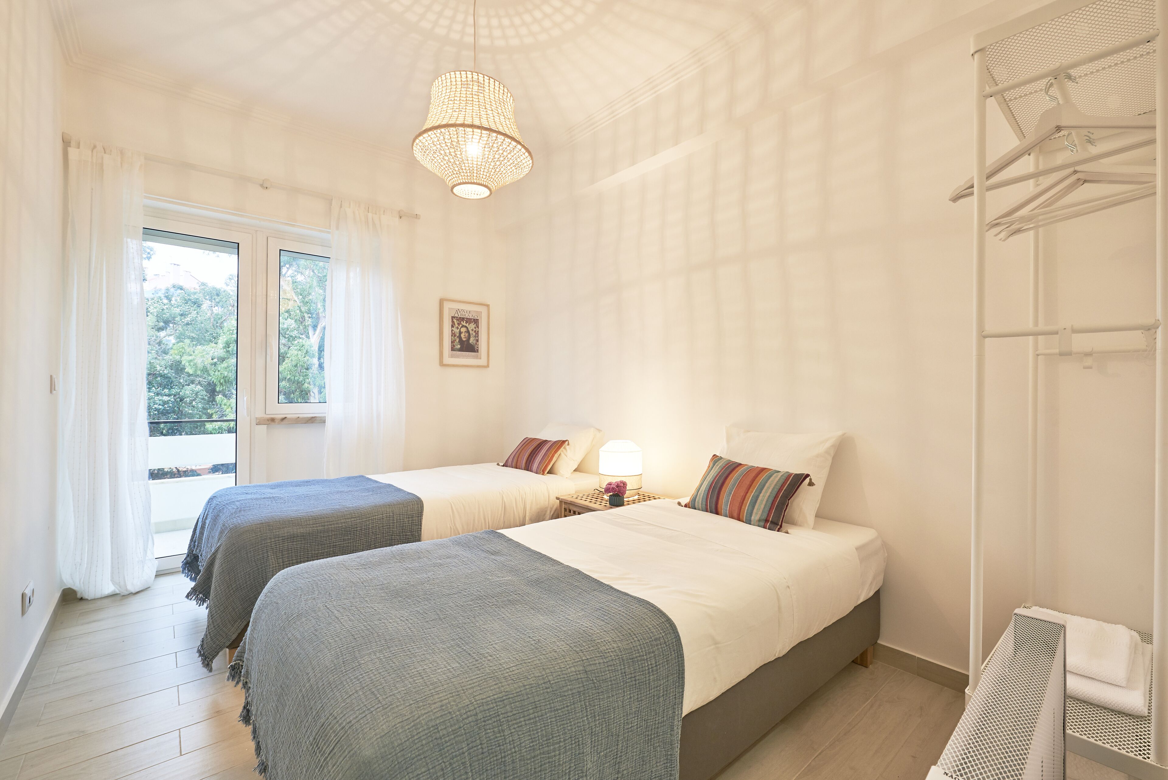 Ett hotellrum med två sängar, en kristallkrona, ett fönster med gardiner och utsikt över grönområden utanför.