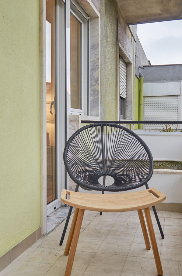Una silla de metal negro con patas y asiento de madera sobre un patio empedrado.