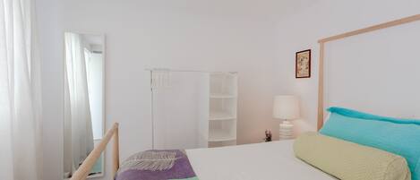 A bedroom with a bed, a nightstand, a lamp, a wardrobe, and a mirror.
