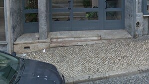A building with a gray entrance featuring a glass door and a small set of steps leading up to it. - Sunny Apartment with Patio, By TimeCooler (Lisbon)