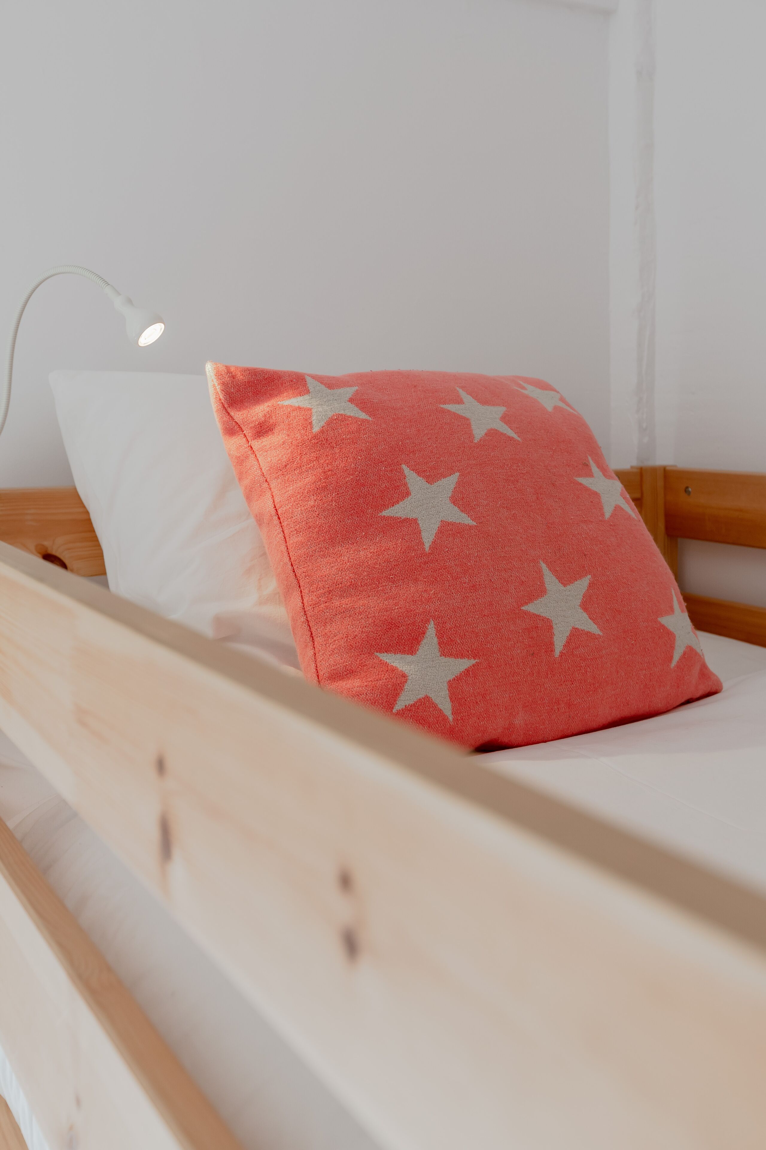 A bed with a wooden frame, a white pillow, and a red pillow with white stars.