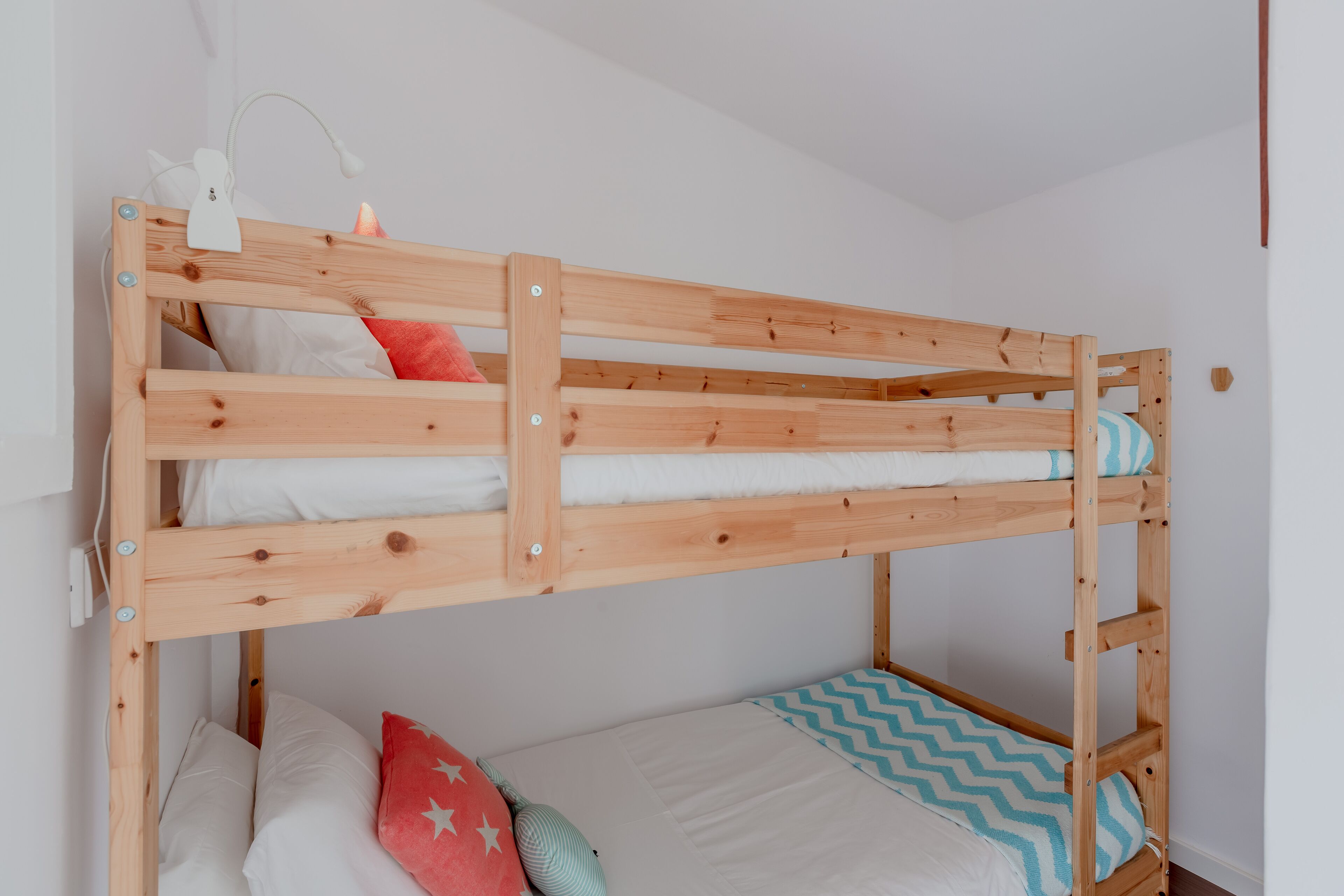 Ein Stockbett mit Holzrahmen, weißer Bettwäsche und einem Kissen mit blau-weißem Zickzackmuster.