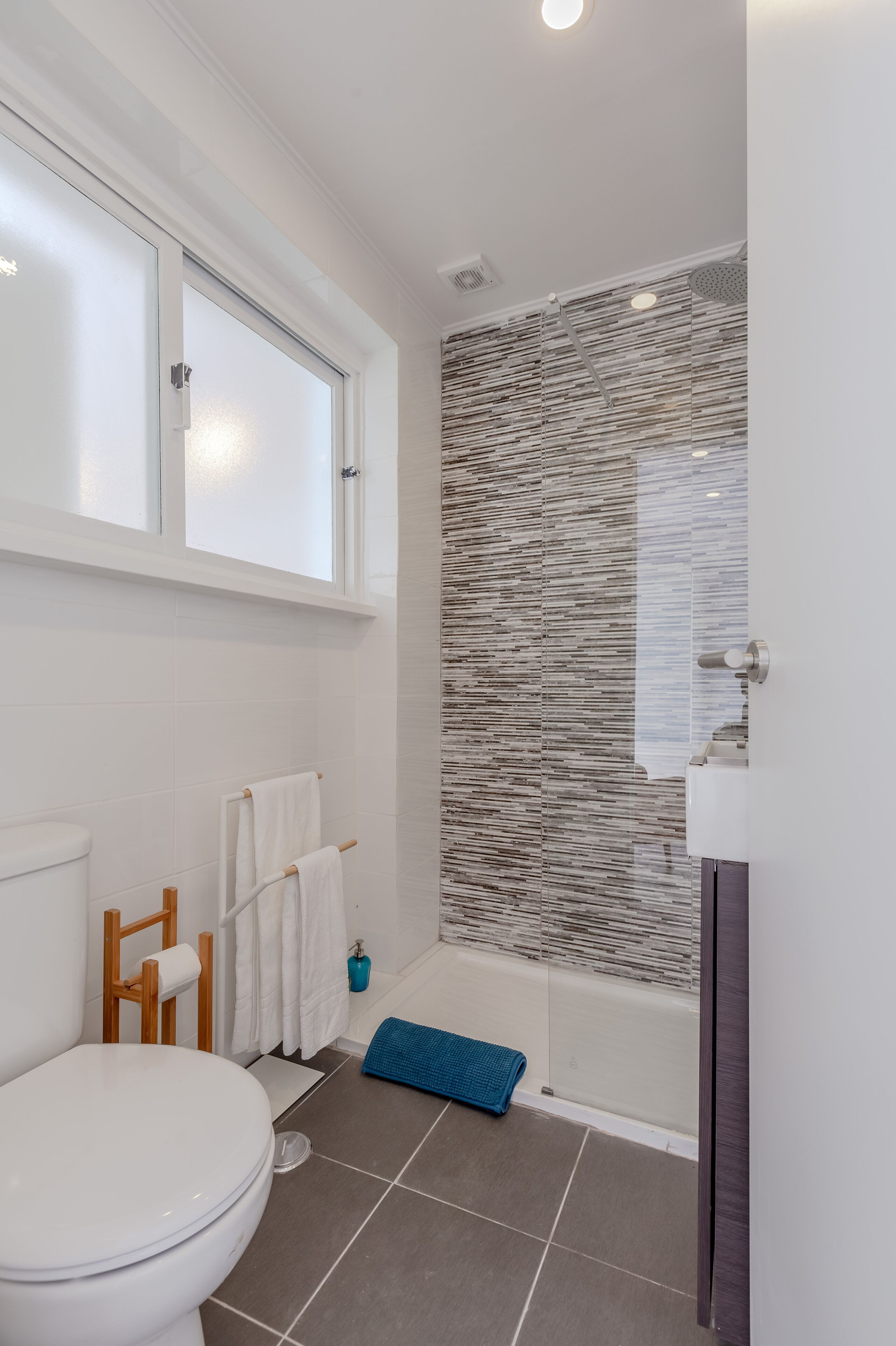 Une salle de bain comprenant des toilettes, une douche avec une porte en verre, une baignoire et une fenêtre située au-dessus des toilettes.