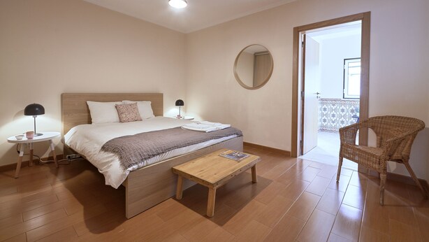 Un dormitorio con cama, mesitas de noche, una mesa de lectura, una silla, un espejo y vistas al balcón.