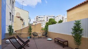 Una terraza en la azotea con piso de madera, dos sillones de descanso, una mesita y una planta en maceta.