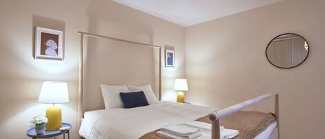 A neatly arranged bedroom with a bed, bedside lamps, a small table with a lamp, and framed pictures on the wall.