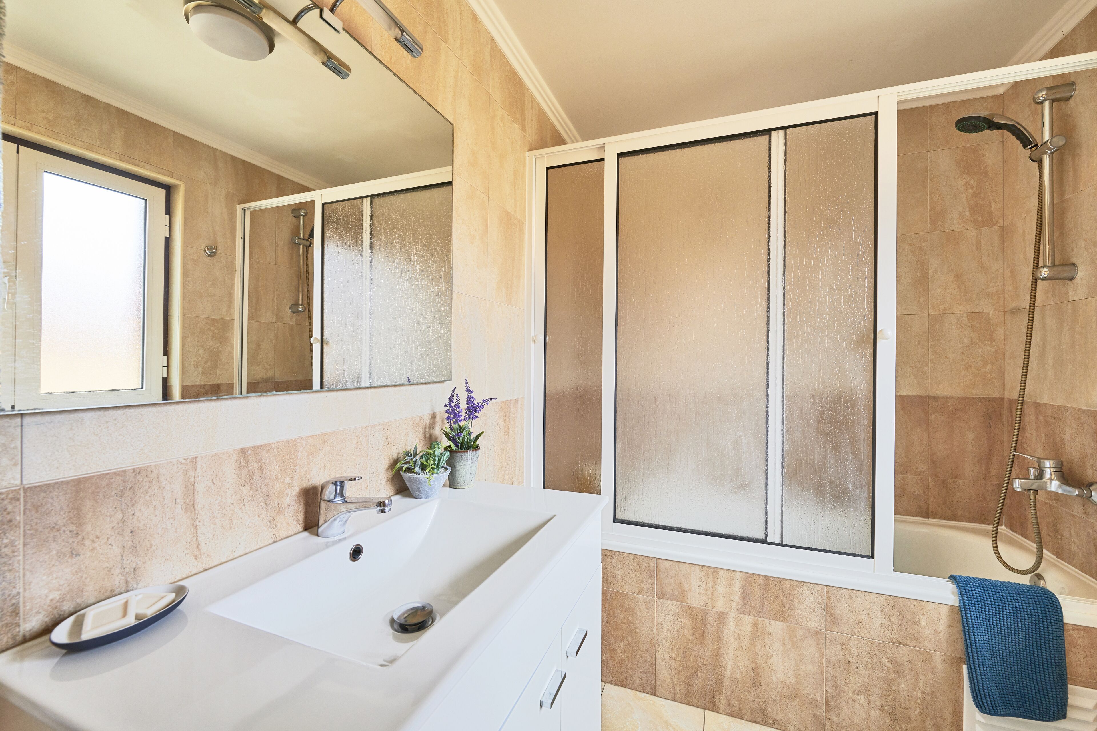 A modern bathroom with a large sink, a shower, and a window.
