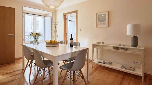 A dining area with a white table, grey chairs, a woven light fixture, and a console table with a lamp.