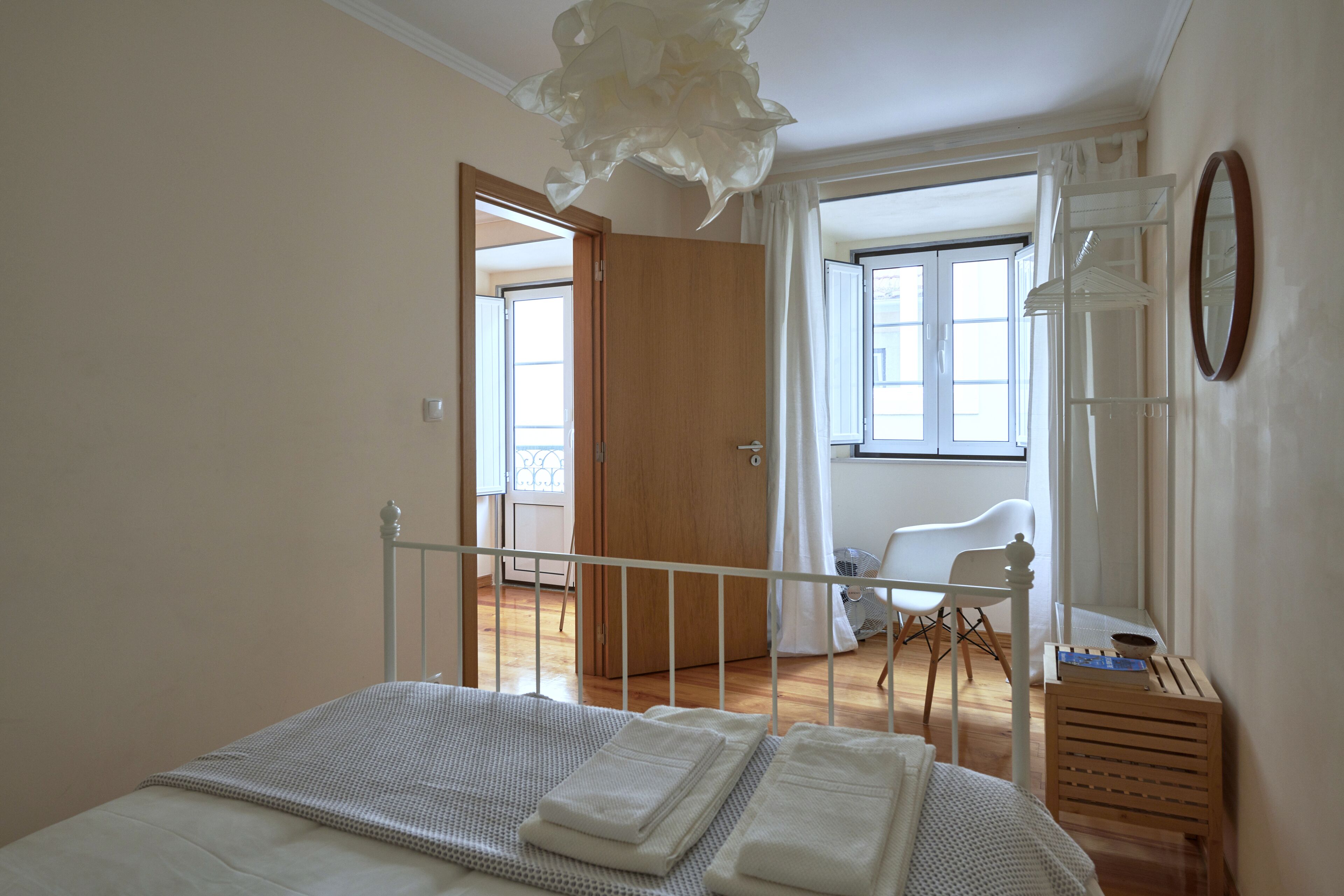 Un dormitorio con cama, un armario de madera, una silla blanca y una ventana con cortinas.