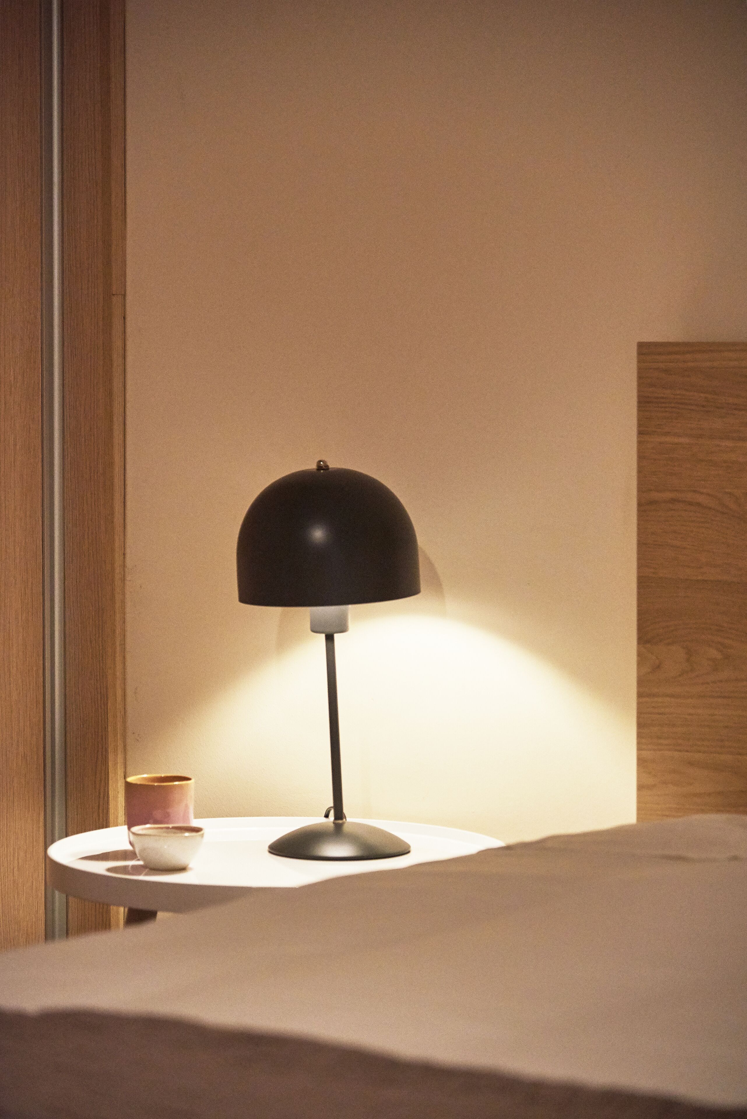 Un comodino con una lampada, una piccola ciotola e una tazza.