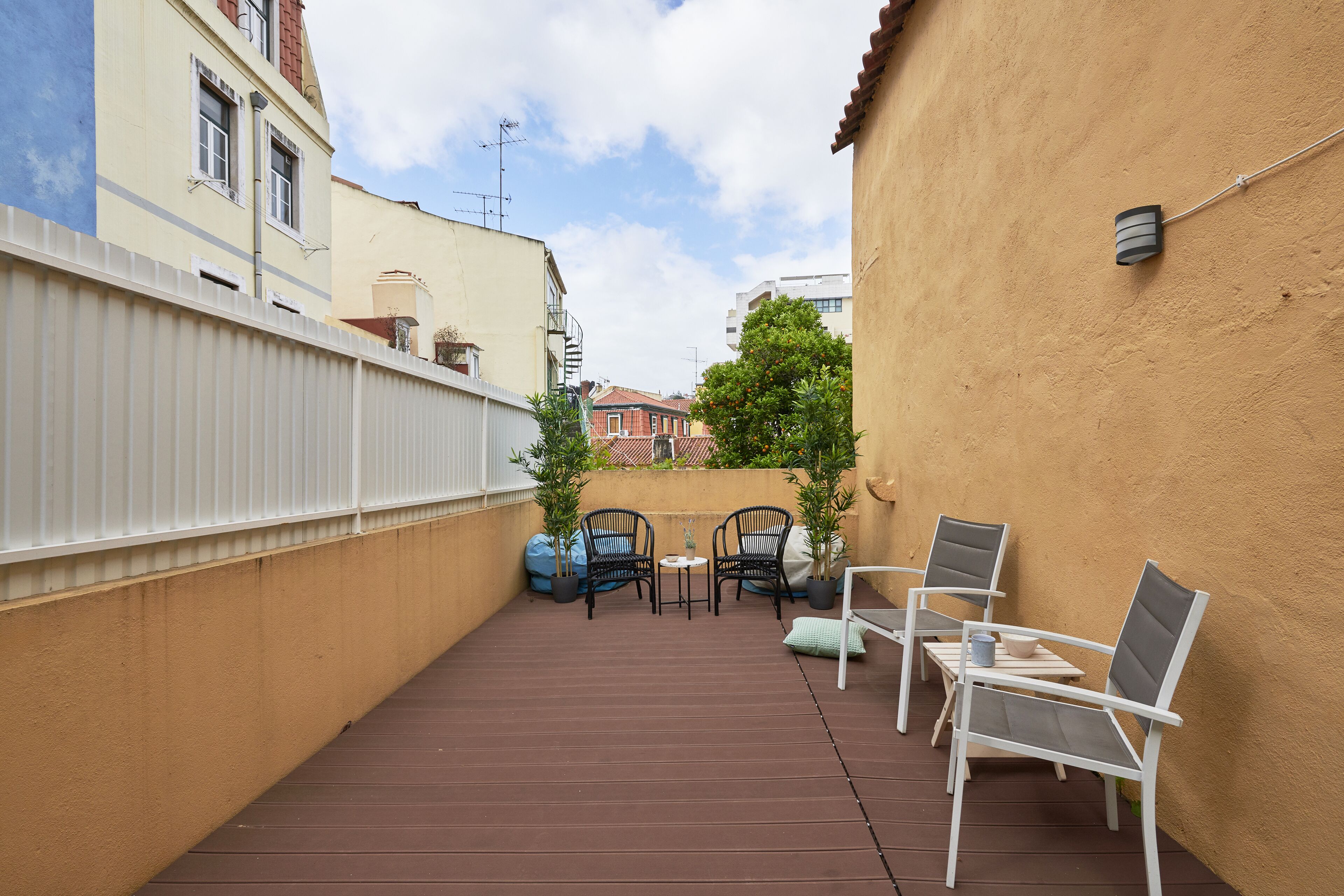 Un pequeño patio al aire libre con piso marrón, baranda blanca y dos mesas con sillas.