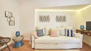 Ein modernes Wohnzimmer mit einem weißen Sofa, Wandbildern und einer blauen Lampe auf einem Beistelltisch.