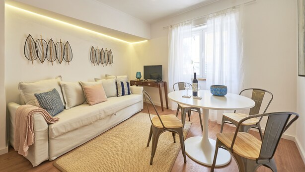 Ein modernes Wohnzimmer mit einer Couch, einem Esstisch und Stühlen. Ein Fernseher und ein dekoratives Wandbild sind ebenfalls vorhanden.