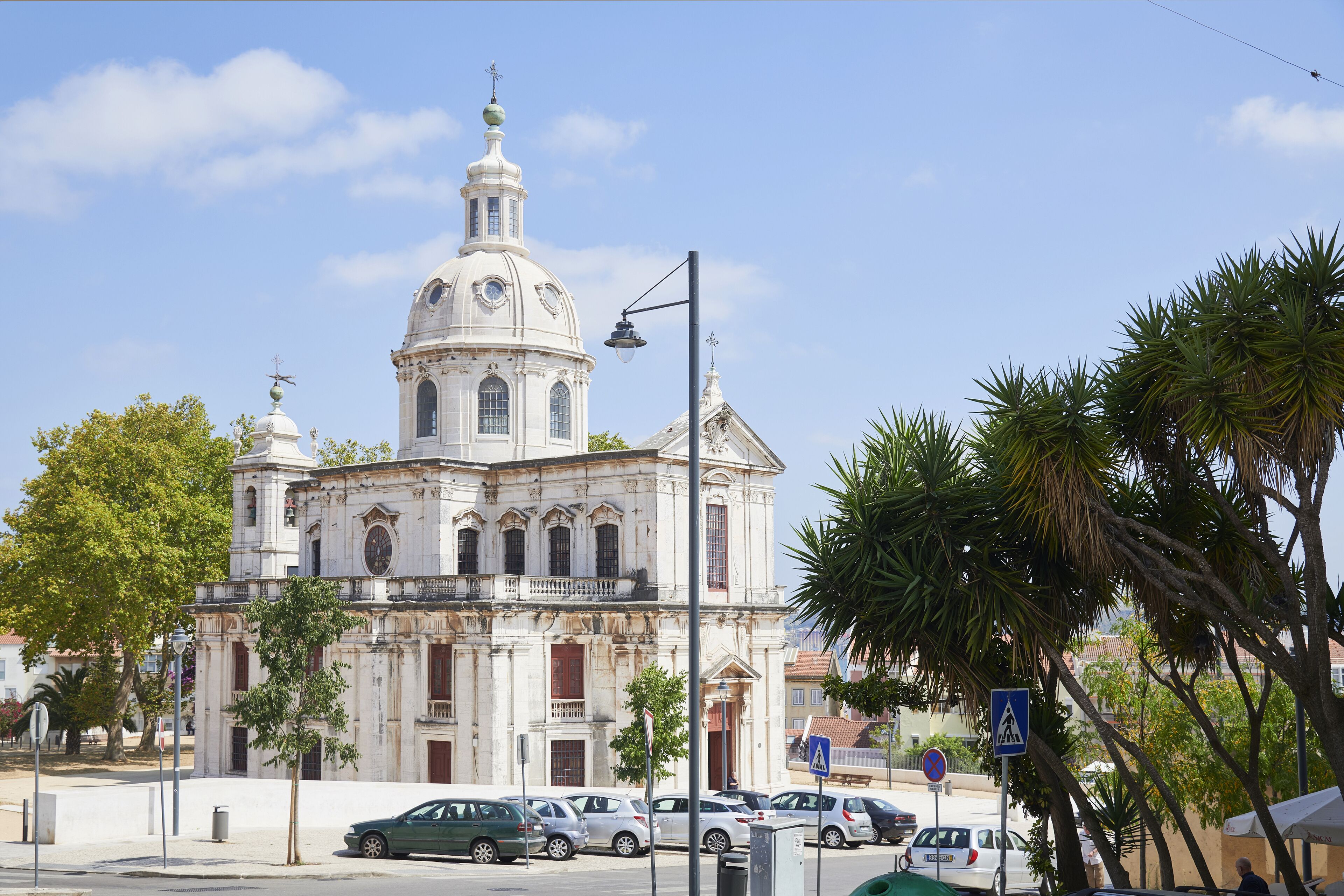 A historic building with a prominent dome and bell tower, surrounded by parked cars and palm trees.