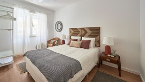 Ein Schlafzimmer mit einem großen Bett, einem Holz-Kopfteil, einem Nachttisch mit Lampe, einem Sessel und einem Kleiderschrank.