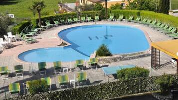 Une piscine dont la surface de l’eau porte l’inscription « HP », entourée de chaises longues vertes et surmontée d’un auvent jaune.