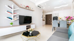 A modern living room with a flat-screen TV, bookshelves, a coffee table, and a dining area with chairs and a table. - Rivergate Residence Apartments (Ho Chi Minh City)