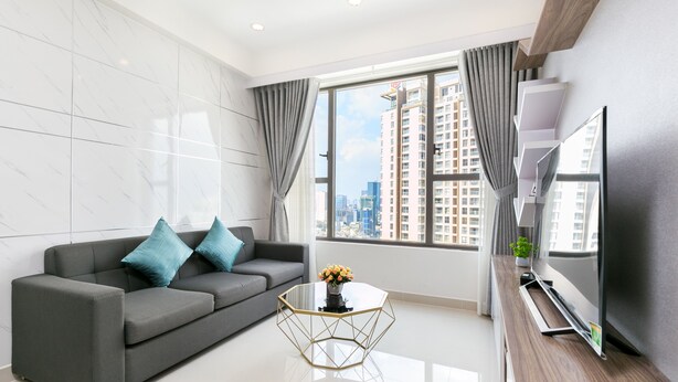 A modern living room with a grey sofa, a glass coffee table, a flat-screen TV, and a large window with curtains. - Rivergate Residence Apartments (Ho Chi Minh City)