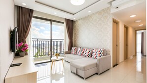 A modern living room with a sofa, a TV, and a balcony with curtains. - Rivergate Residence Apartments (Ho Chi Minh City)