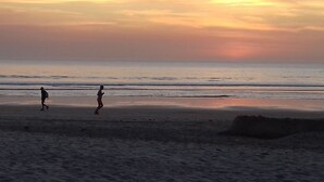 A beach scene with two people running along the shore during sunset. - Kounakito - Meaning 'welcome' (Oussouye)