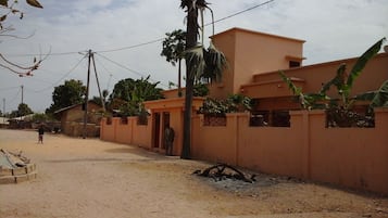 Una zona residencial con una casa de dos pisos, una calle pavimentada y una persona de pie cerca de la entrada.