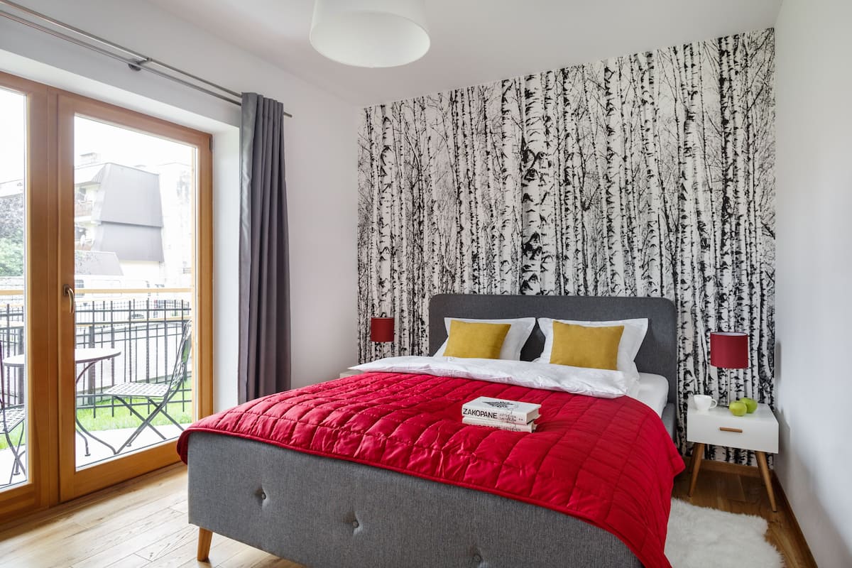 A bedroom with a bed, a nightstand, a window, and a view of the outside.