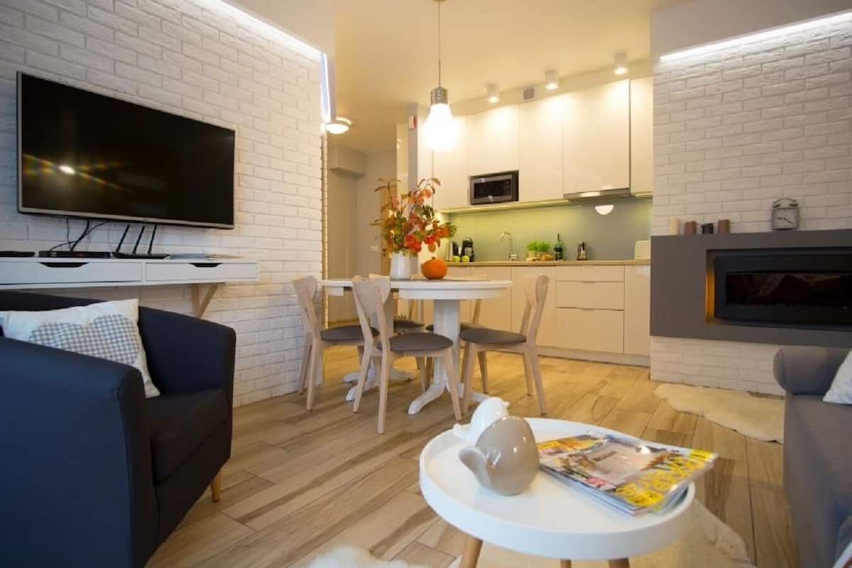 A modern living room with a flat-screen TV, a sofa, a dining table with chairs, and a fireplace.