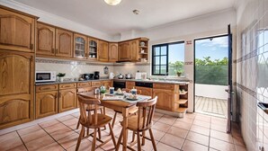 Une cuisine avec des meubles en bois, une table à manger avec des chaises, et une vue sur l’extérieur grâce à une porte coulissante.
