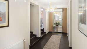 Um corredor moderno com um candelabro, um quadro na parede e uma escada que leva a outro cômodo.