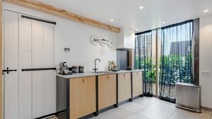 Eine moderne Küche mit einer zentralen Kochinsel, einer Spüle und einem Kühlschrank. Holzschränke und ein großes Fenster mit leichten Vorhängen.