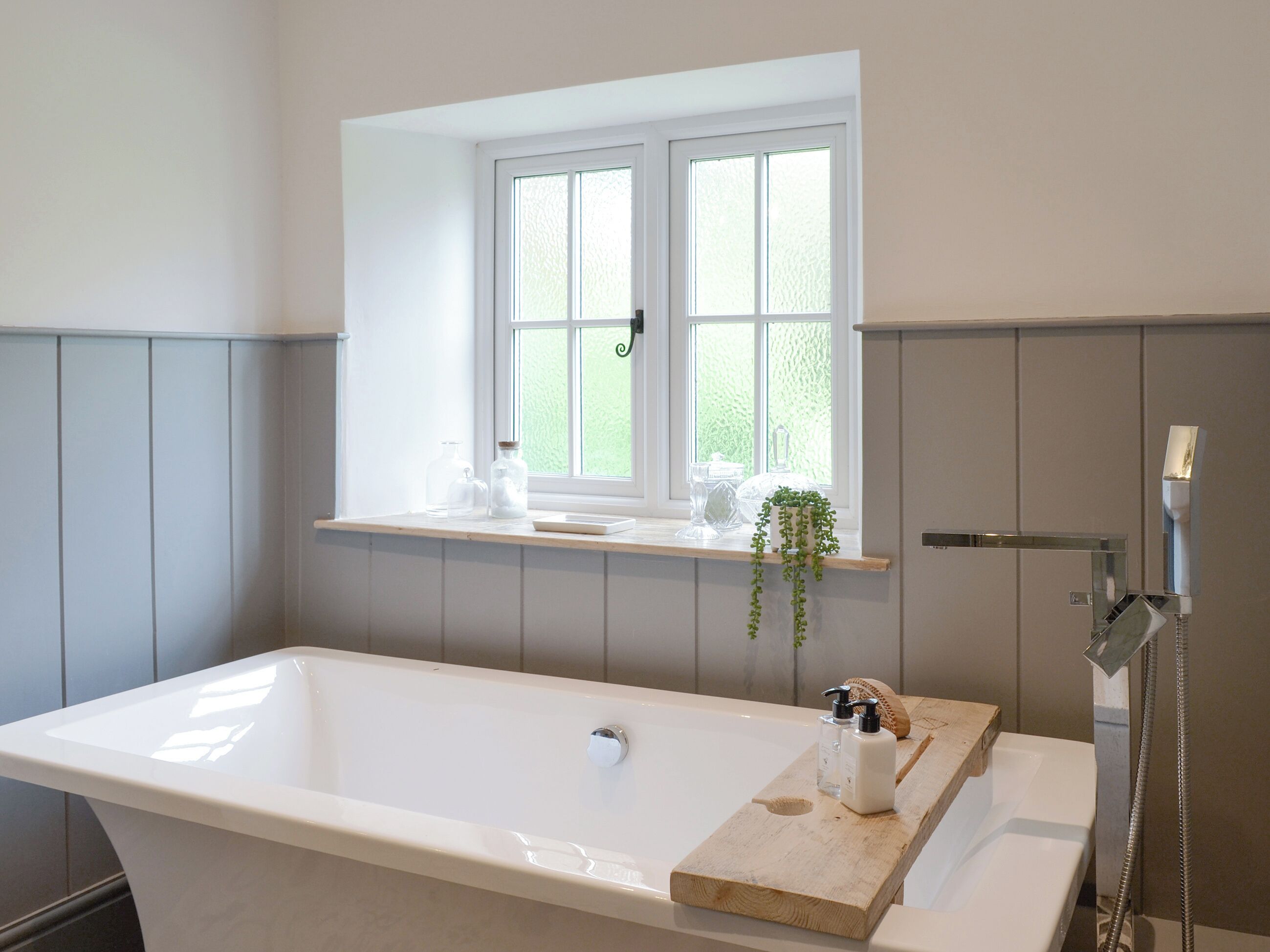 Ein modernes Badezimmer mit einer freistehenden Badewanne, einem Fenster über dem Waschbecken und einer Holzablage mit Pflegeprodukten.