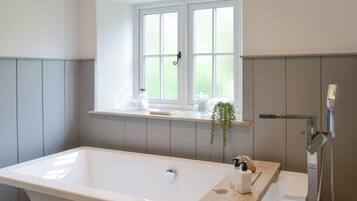 Ein modernes Badezimmer mit einer freistehenden Badewanne, einem Fenster über dem Waschbecken und einer Holzablage mit Pflegeprodukten.