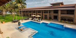 A pool area with lounge chairs and umbrellas, surrounded by a building with a tiled roof and multiple balconies. - Marquis Beach Resort (Candolim)