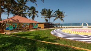 Un hotel frente a la playa con un mural colorido, un área de diseño circular y palmeras.