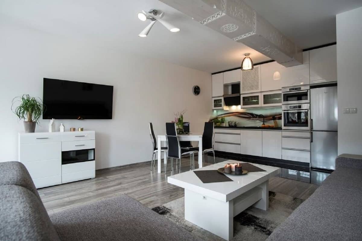 A modern living room with a flat-screen TV, a dining area, and a kitchen with stainless steel appliances.
