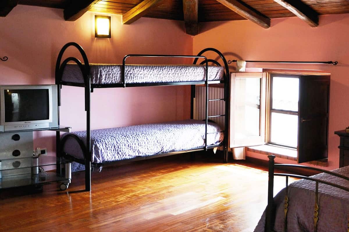 A room with bunk beds, a television, a window, and a bedside table with a lamp.