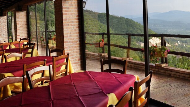 A restaurant with tables set for dining, a brick wall, and a view of a mountainous landscape. - Fattoria Alvaneta (Padula)