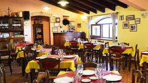 A restaurant with multiple tables, each set with wine glasses and plates, and a bar area with shelves and a clock. - Fattoria Alvaneta (Padula)