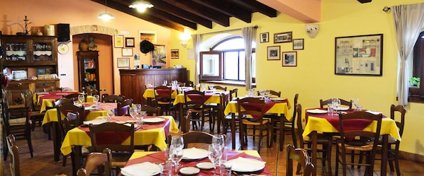 Un restaurante con varias mesas, cada una con copas de vino y platos, y una zona de bar con estanterías y un reloj.