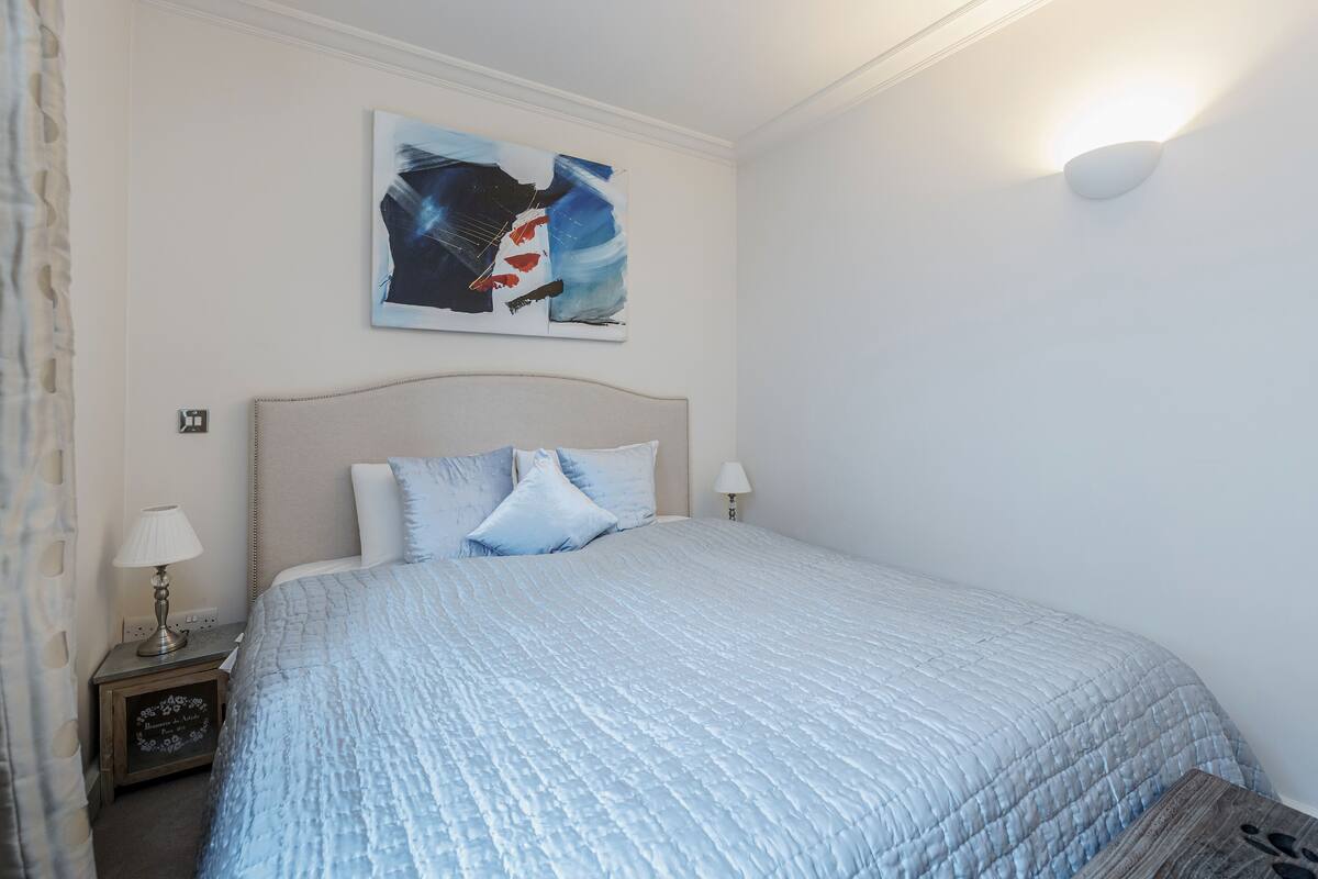 A neatly made bed with a textured blue duvet, a headboard, and two bedside lamps.