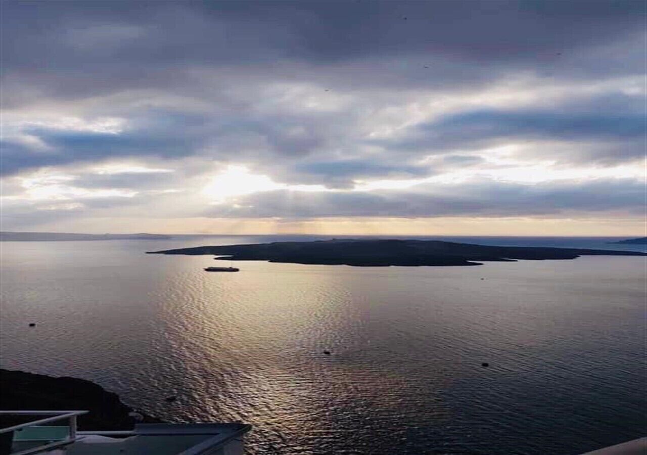 A coastal view with calm waters and a distant landmass under a cloudy sky.