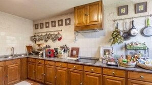 Una cocina con armarios de madera, un lavamanos de acero inoxidable y diversos utensilios y electrodomésticos.