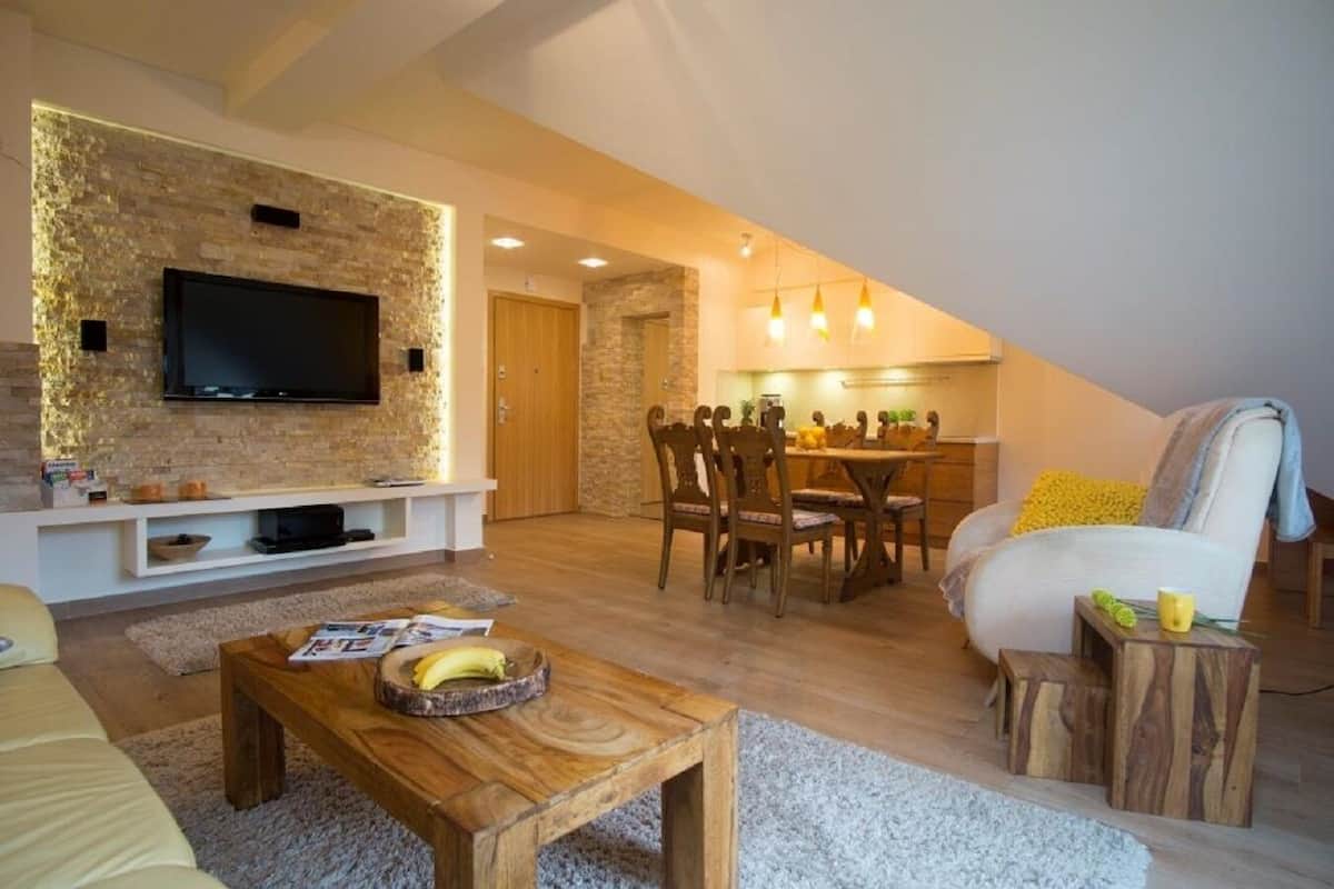 Uma sala de estar moderna com televisão de tela plana, móveis de madeira e um espaço de jantar com cadeiras e uma mesa.