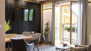 Een moderne woonkamer met een eethoek, een aan de muur bevestigde televisie en een balkon met uitzicht.