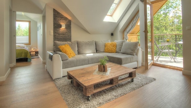 Een slaapkamer in loftstijl met een schuine kap, een inbouwkruk en een groot raam met uitzicht op een balkon.