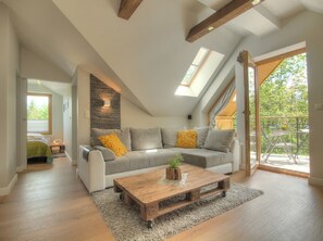 Une chambre de style « loft » avec un plafond en pente, un banc intégré et une grande fenêtre donnant sur un balcon.