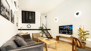 En moderne stue med sofa, sofabord og fjernsyn. Der er trapper, der fører til et andet niveau, og en plante til højre.