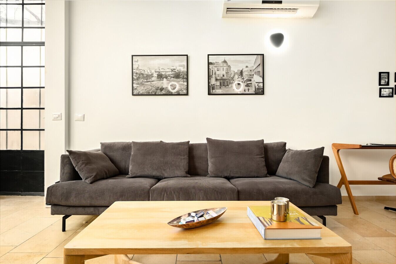 Un salon moderne avec un canapé gris, une table basse en bois et deux photographies en noir et blanc accrochées au mur.